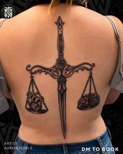 Sword and scales back piece in black and grey realism, tattooed by Aaron Noble