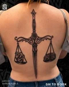 Sword and scales back piece in black and grey realism, tattooed by Aaron Noble